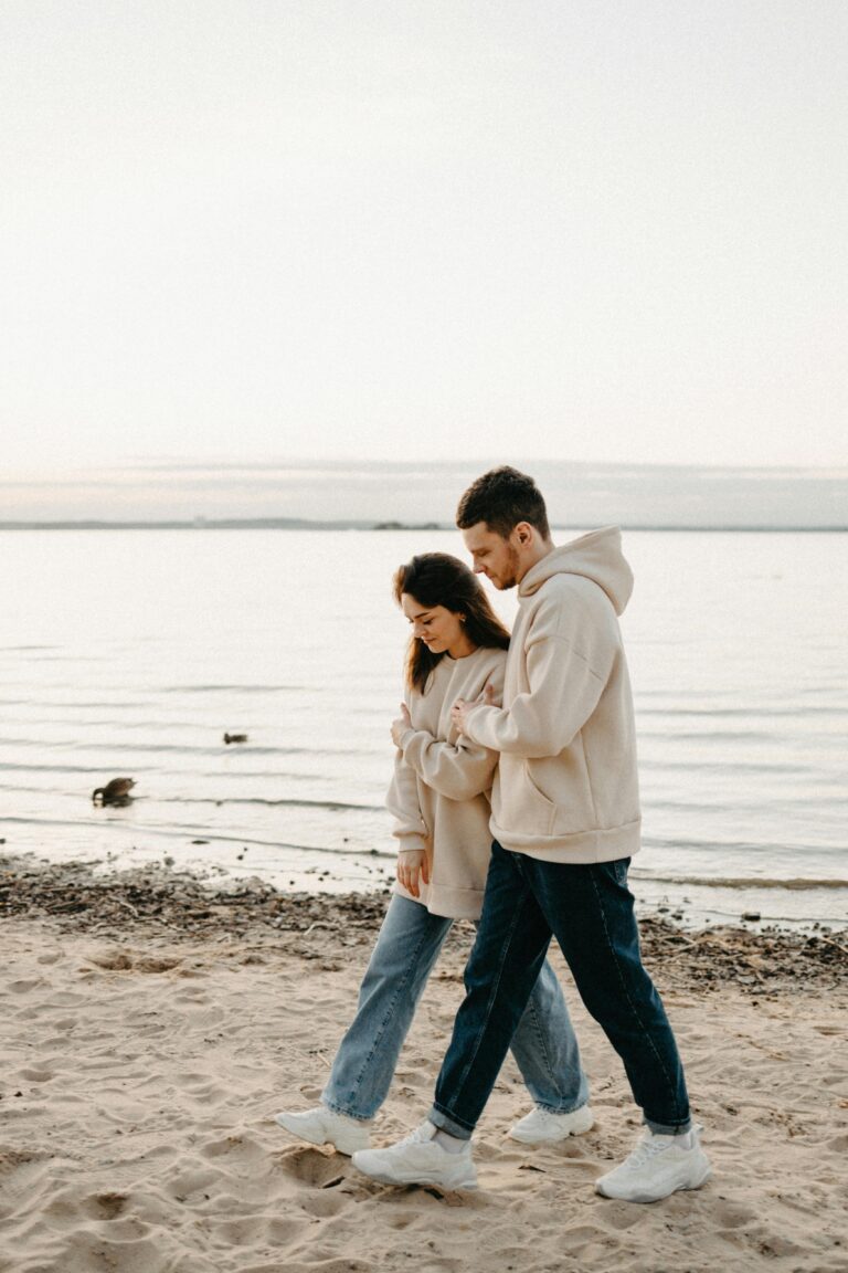 A loving couple walks hand in hand along a tranquil beach during sunset.